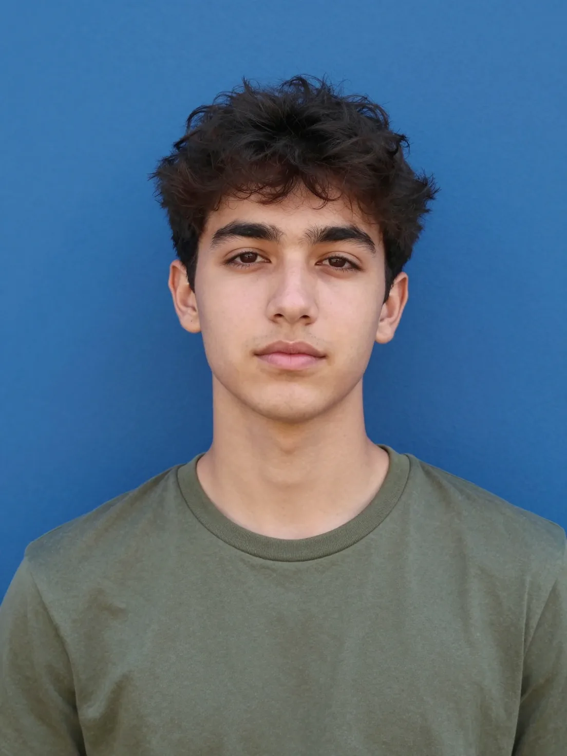 A young man with dark, textured hair poses for a centered...